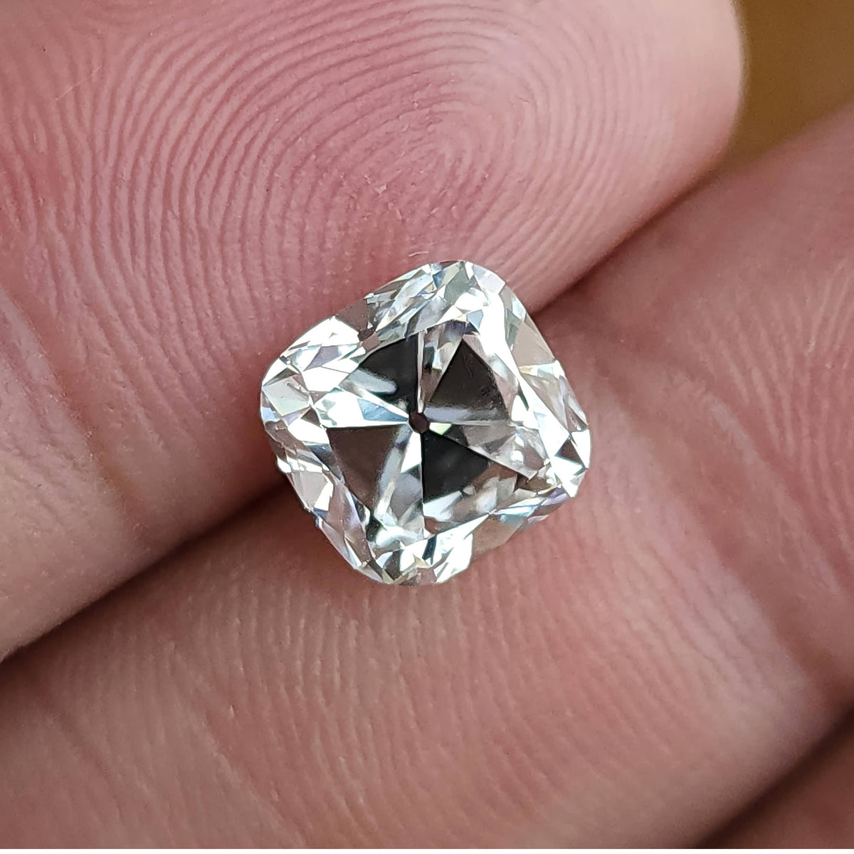 Square cushion cut loose stone shown on fingertips highlighting clear body color and proportions.