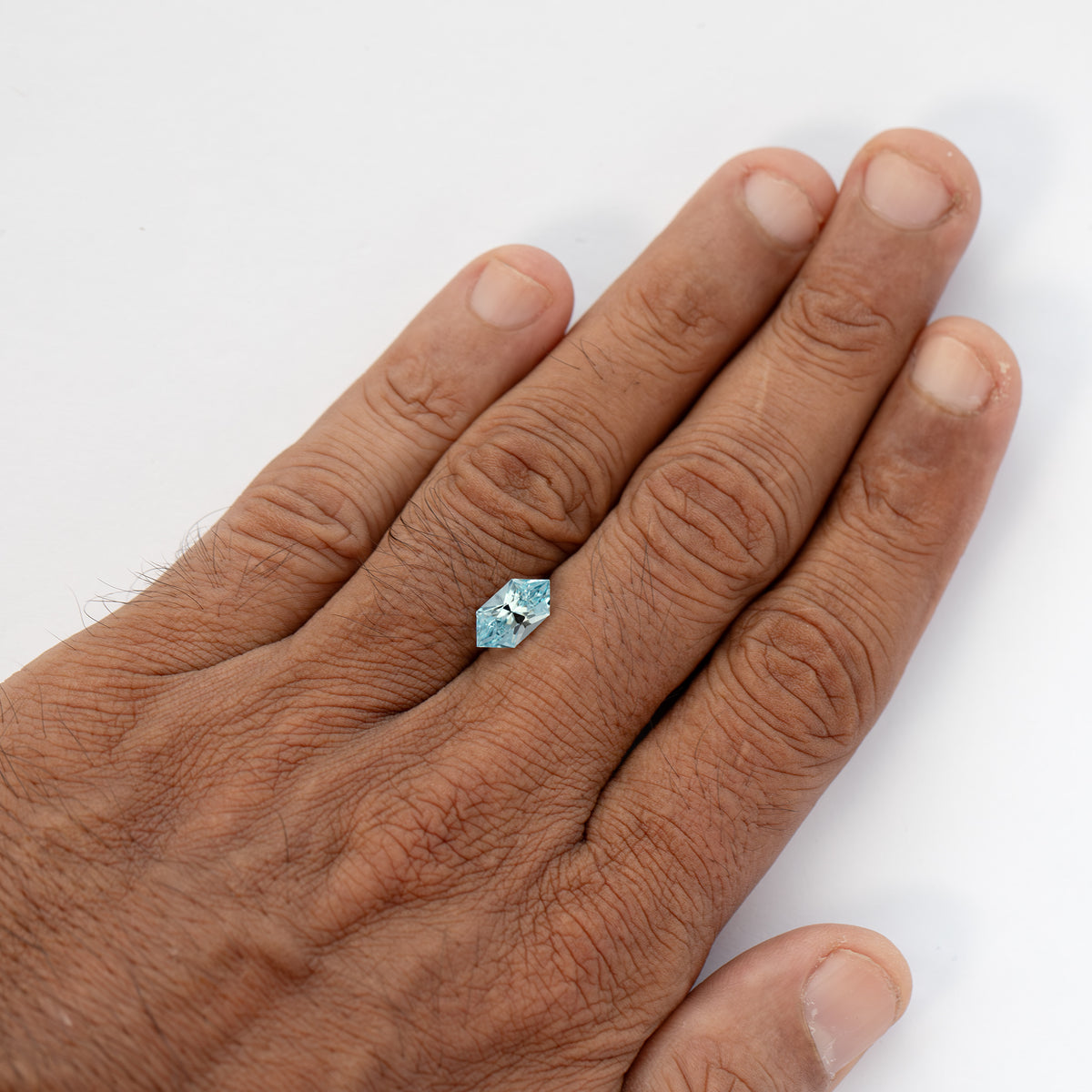 A second hand-held size-reference view of the pale-blue loose sapphire.