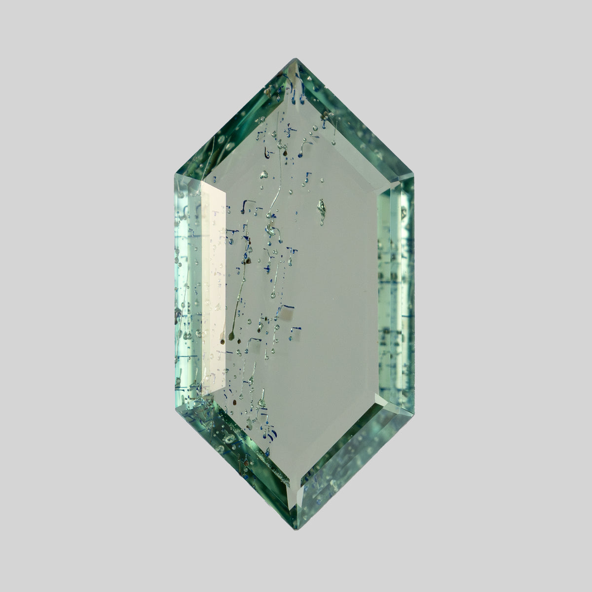 Face-up view of elongated hexagonal portrait cut green gemstone on plain light grey background.