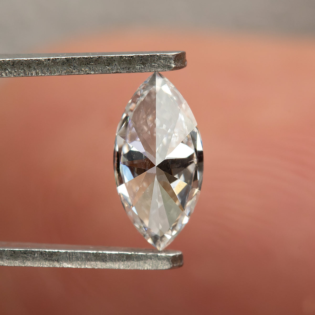 Reverse-facing marquise diamond in tweezers, showing broad pavilion facets meeting along the long center line.