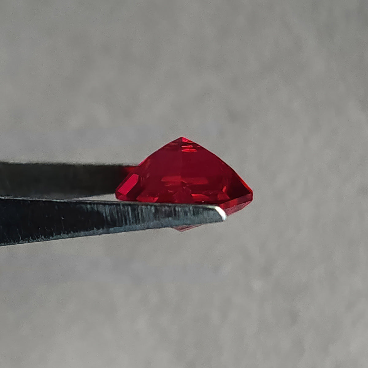 Side profile of a kite-shaped lab-grown ruby in tweezers, showing its crown and pavilion depth.