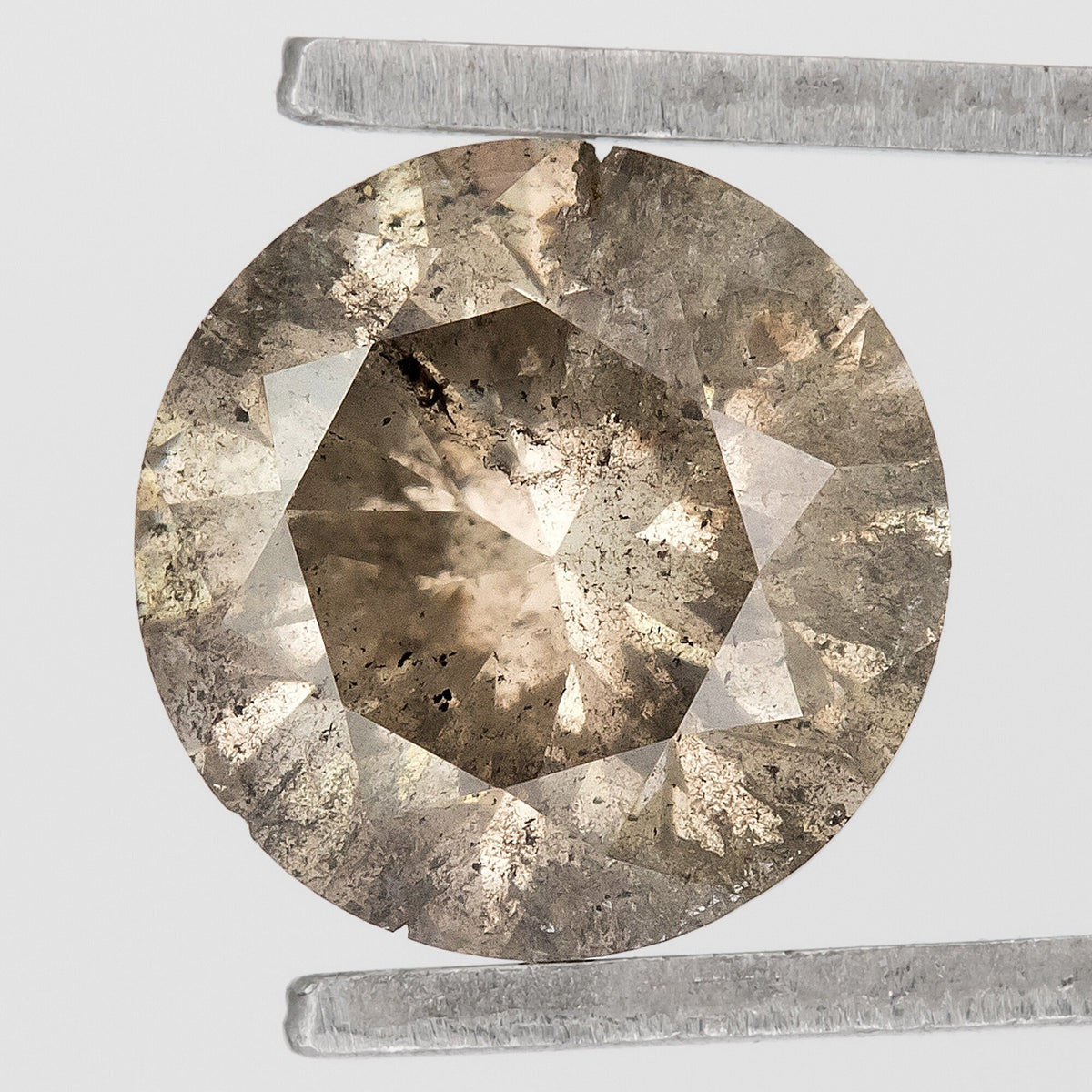 Face-up macro of the champagne-brown round diamond in tweezers, with numerous dark and pale inclusions and visible edge irregularities.