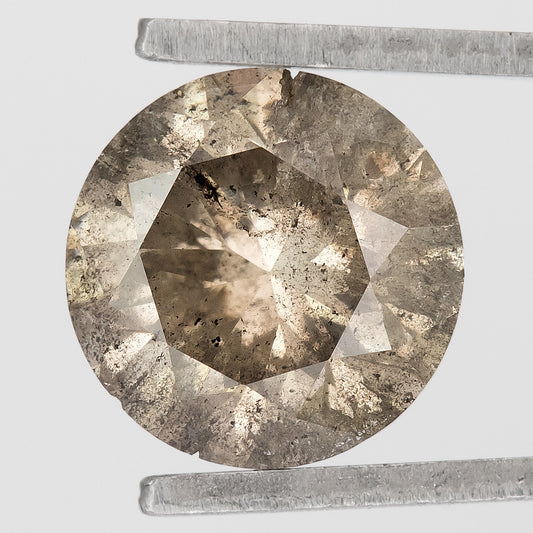 Face-up macro of the champagne-brown round diamond in tweezers, with numerous dark and pale inclusions and visible edge irregularities.