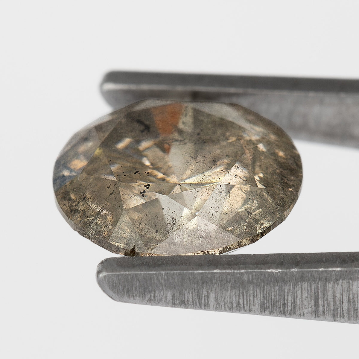 Champagne-brown round diamond tilted in tweezers, showing its table, crown facets and dense internal characteristics.