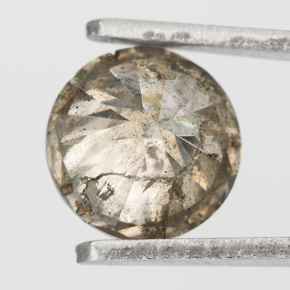 Back view of the champagne-brown round diamond in tweezers, showing pavilion facets and prominent dark and pale inclusions.