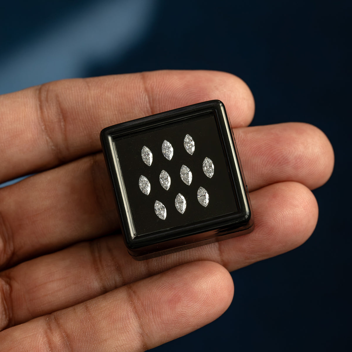 Black marquise-diamond display box held across the palm for scale; the pictured parcel is a supply reference.