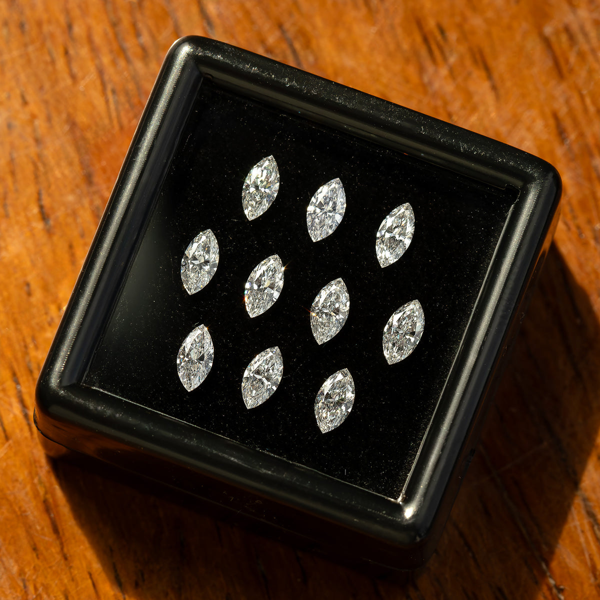 Black display box of marquise diamonds on a warm wooden surface, with individual stones catching different reflections.
