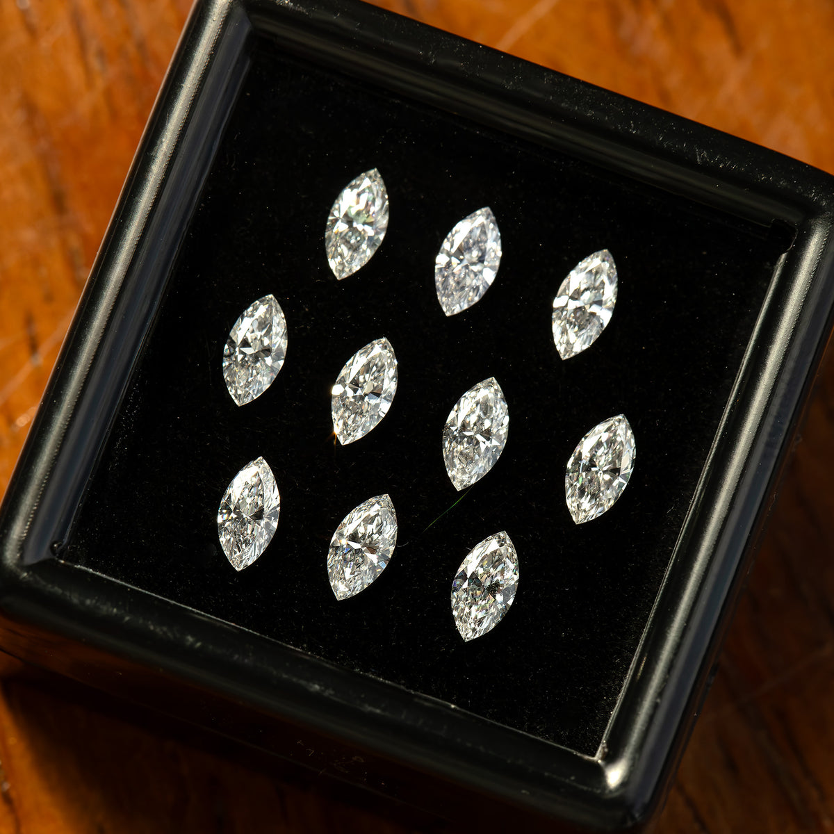 Angled close-up of marquise diamonds in their black display box on wood, showing brilliant-facet reflections.
