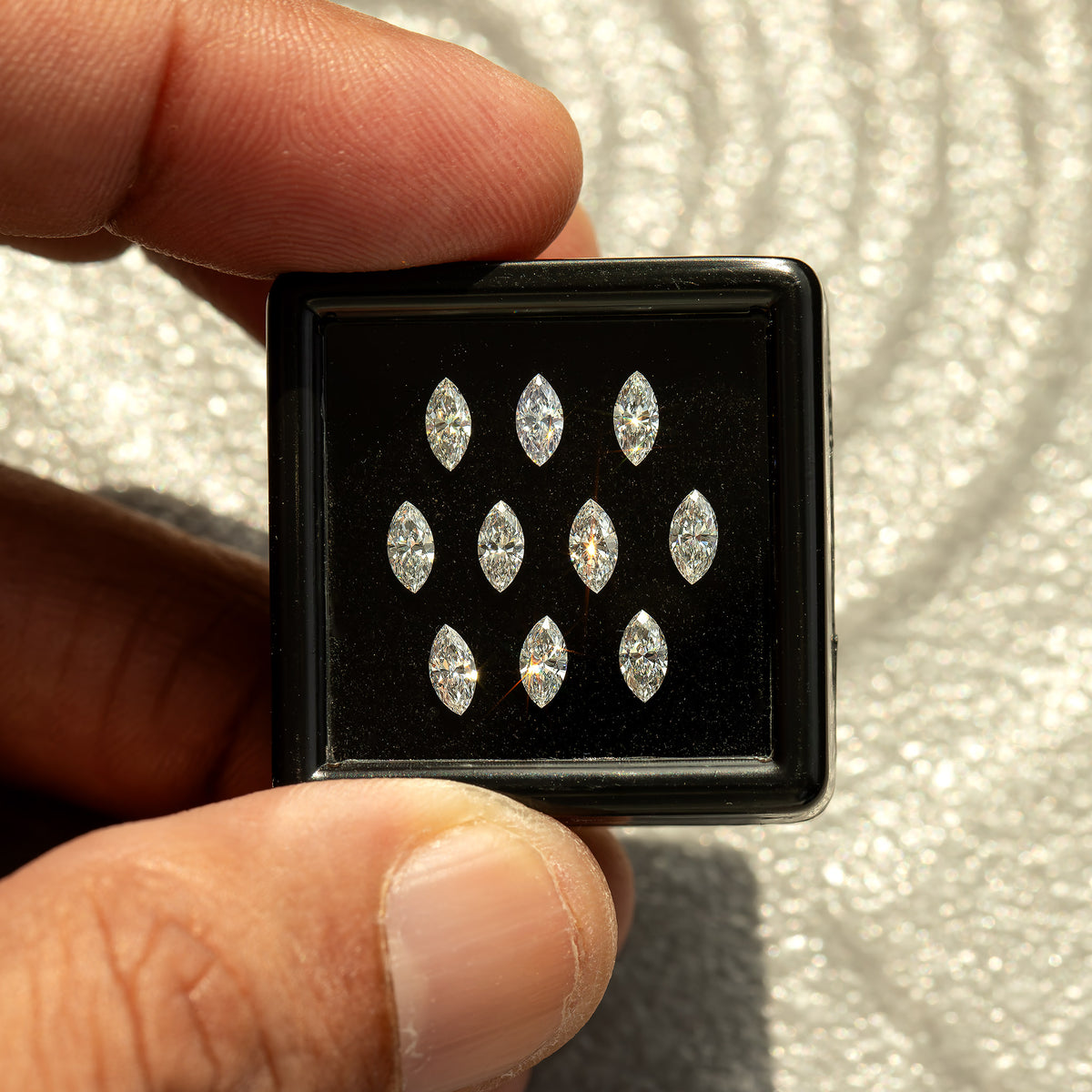 Marquise-diamond display box held at its corners between fingertips, showing the size of the reference parcel.