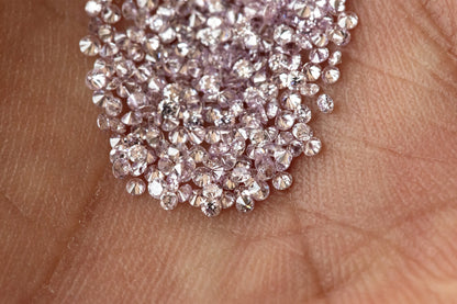 Representative purple-pink round diamond melee on an open palm for scale; one order is five stones.