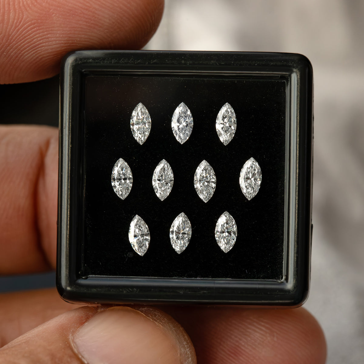Front view of ten marquise diamonds in a display box held in one hand, with skin behind the black box.