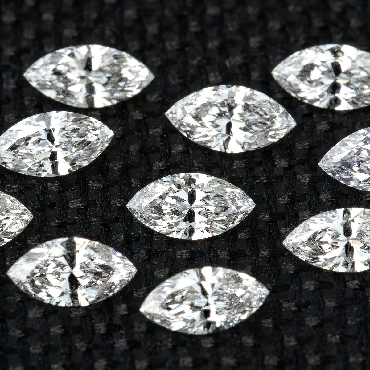 Close macro of loose marquise diamonds on black woven fabric, showing bright facets and dark reflected areas.