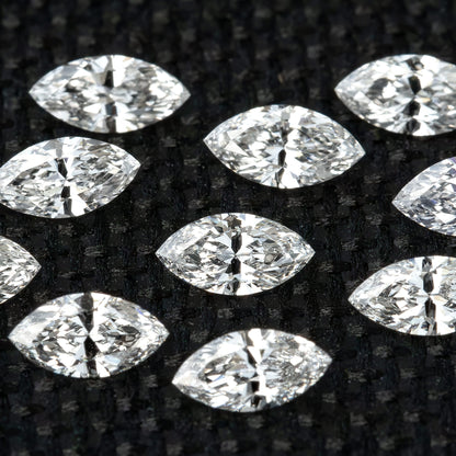 Close macro of loose marquise diamonds on black woven fabric, showing bright facets and dark reflected areas.