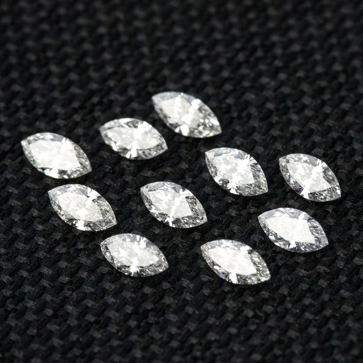 Angled layout of ten loose marquise diamonds on black fabric, with different tilts showing facet reflections.