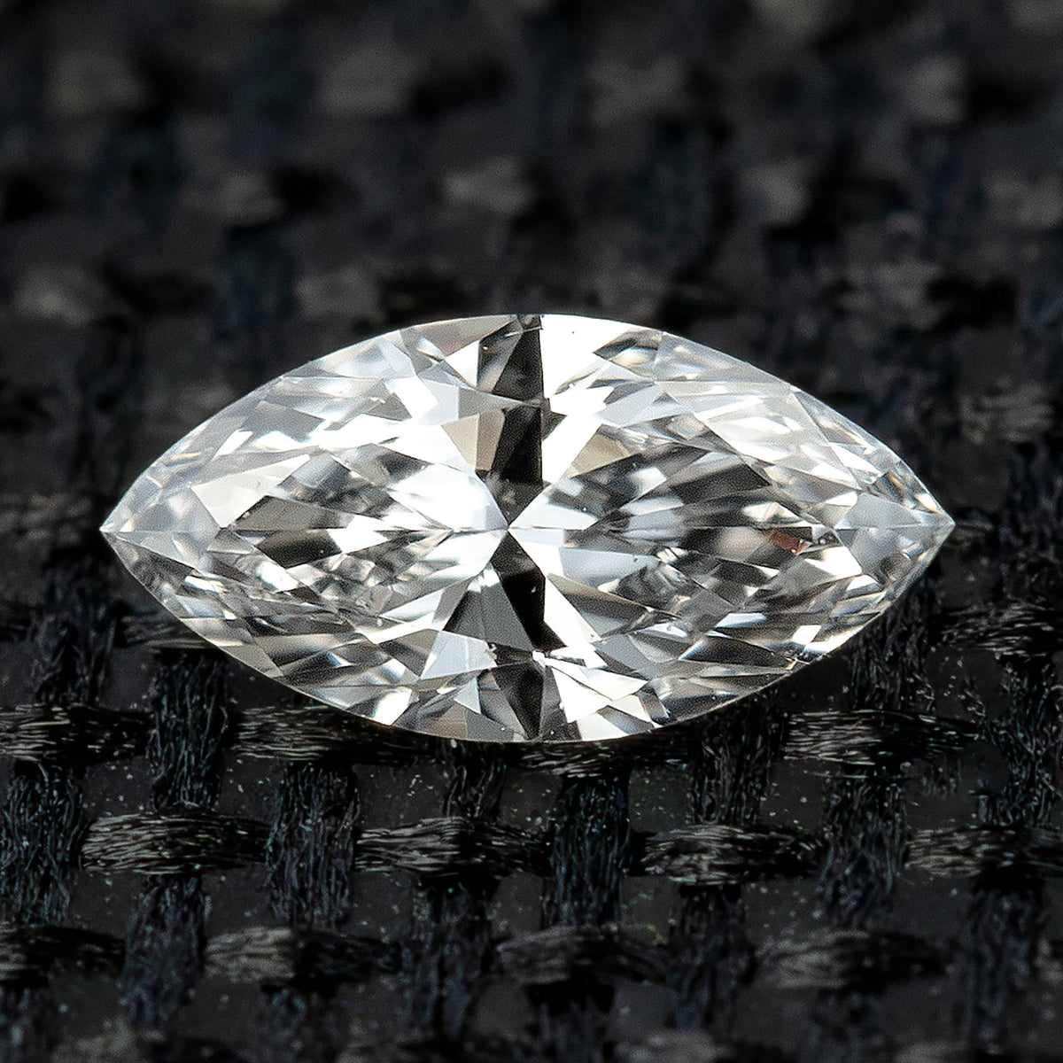 One 5x2.5 mm marquise natural diamond photographed face-up on black woven fabric, showing its pointed outline and brilliant facets.