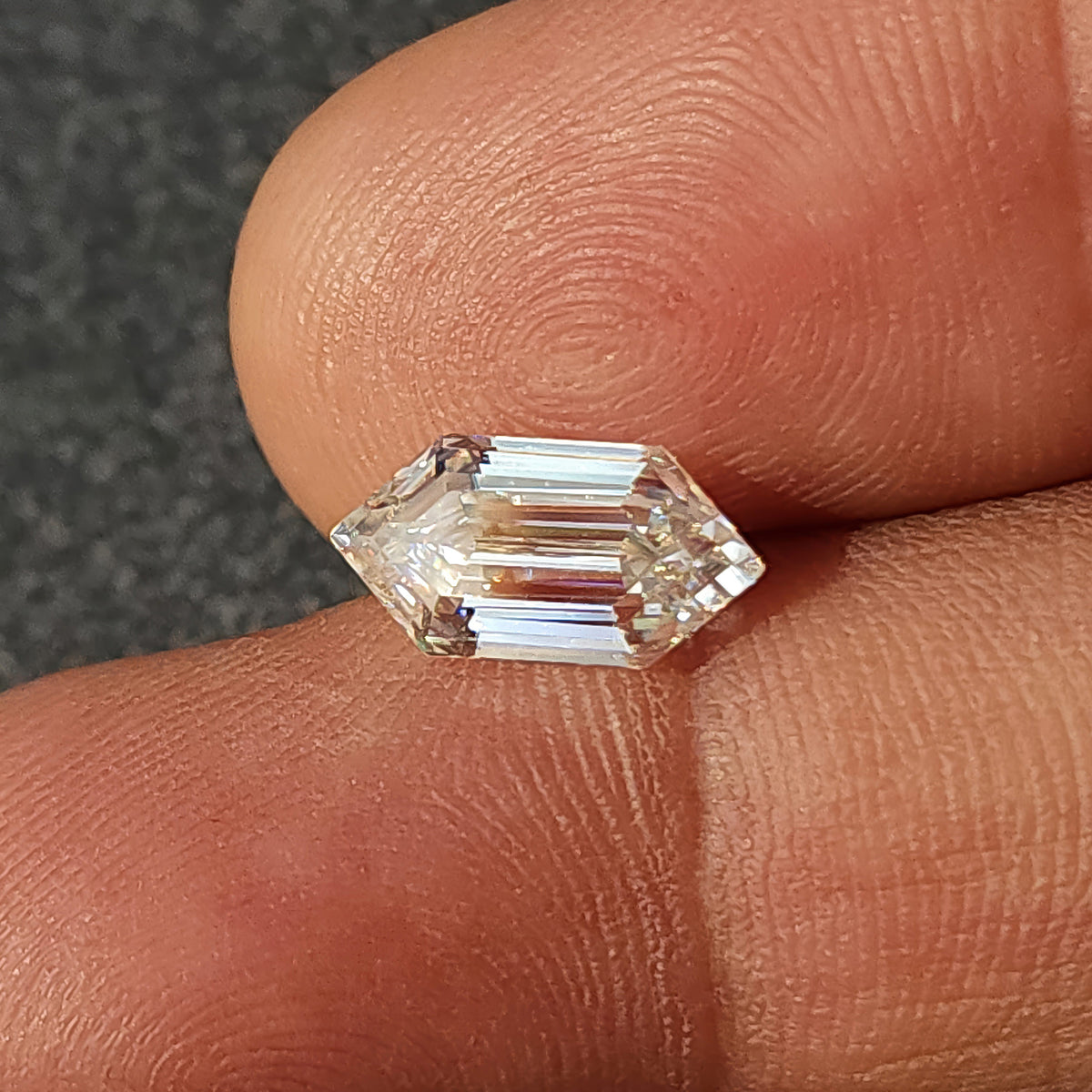 Elongated hexagon step-cut gem resting horizontally on fingers showing hand scale and step faceting.