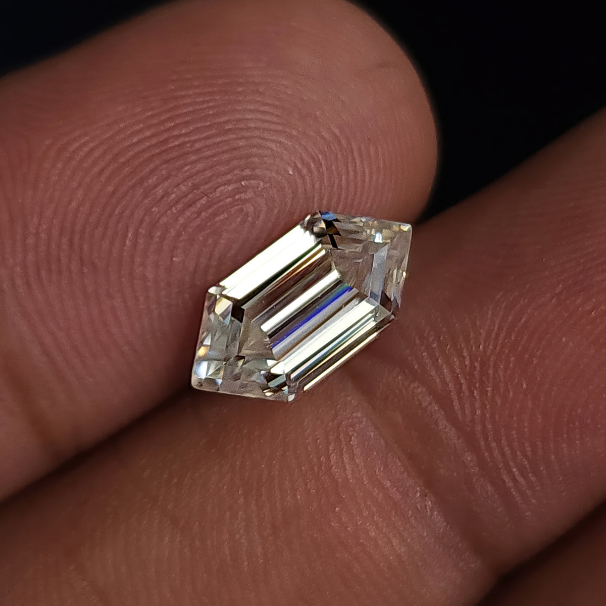 Angled view of an elongated hexagon step-cut gemstone resting on fingers displaying reflective facet pattern.