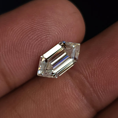 Angled view of an elongated hexagon step-cut gemstone resting on fingers displaying reflective facet pattern.