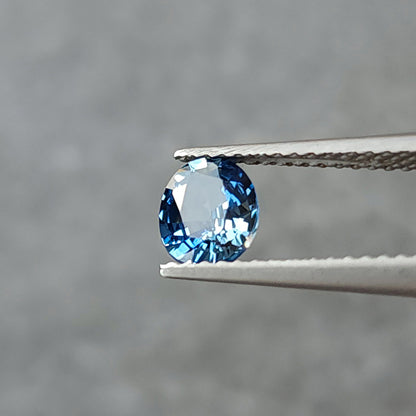 Tilted oval sapphire in tweezers, showing a broad pale reflection across the central facets.