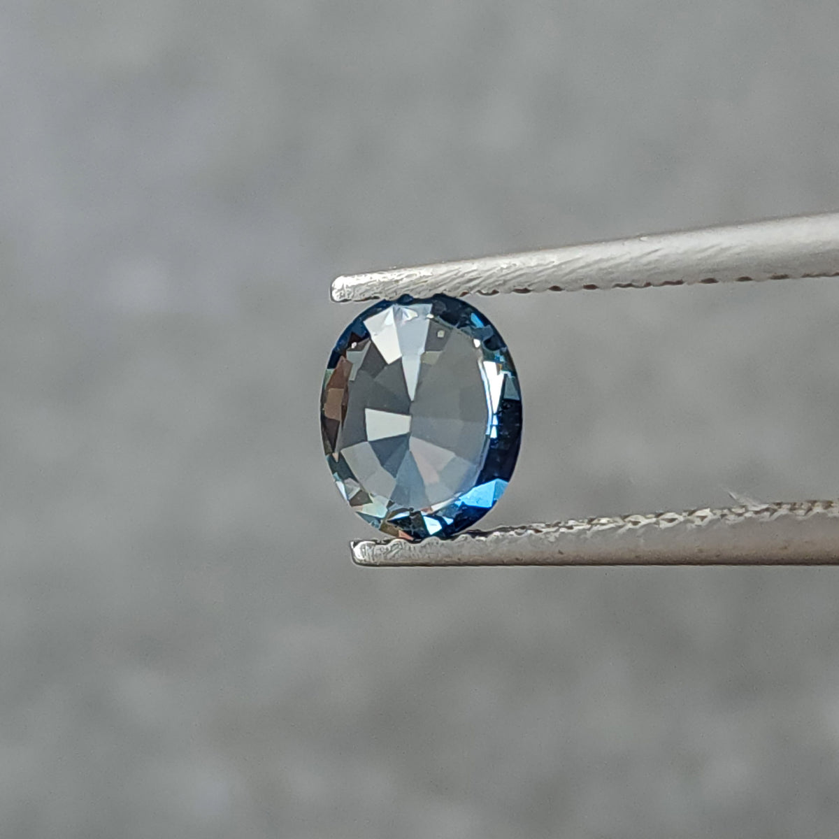 Rotated tweezers view of the oval sapphire with broad gray facet reflections.
