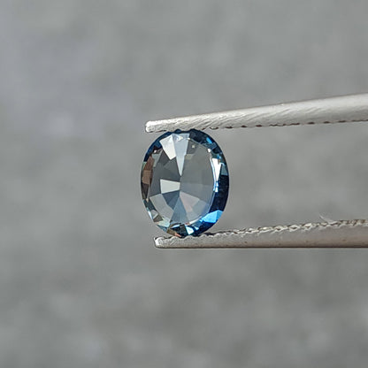 Rotated tweezers view of the oval sapphire with broad gray facet reflections.