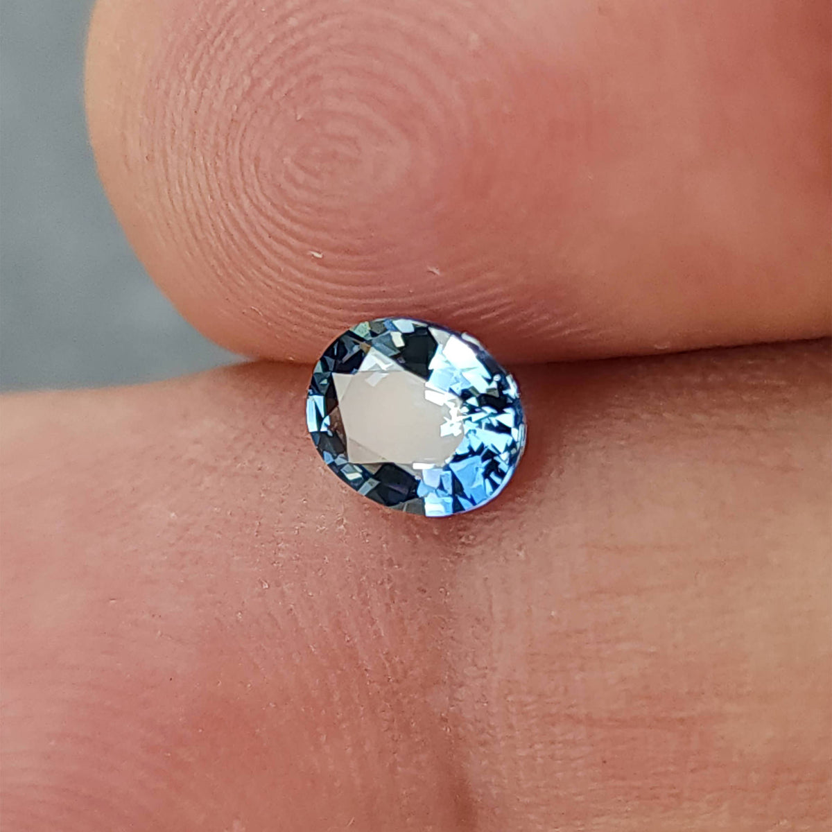 Alternate fingertip view of the oval sapphire with a bright pale reflection at the center.