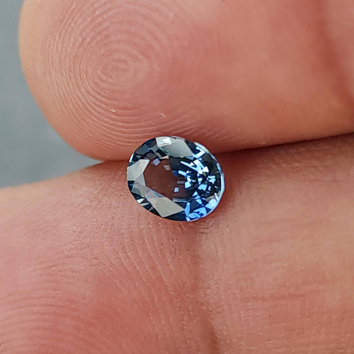 Close face-up view of the oval sapphire between fingertips, showing alternating blue and dark reflections.
