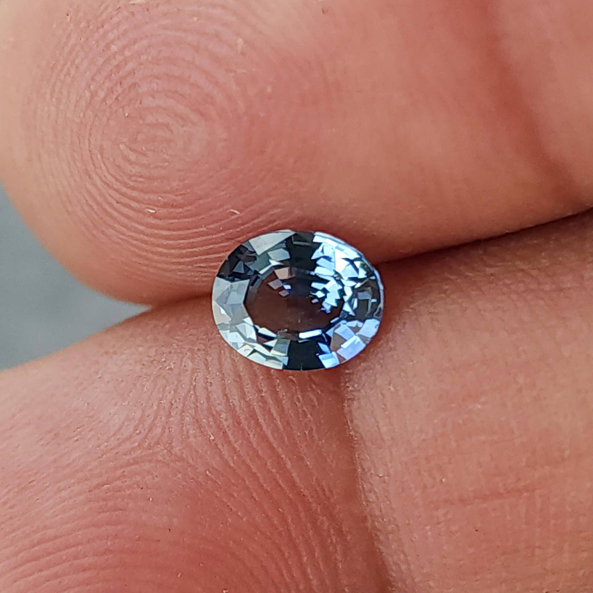 Wider fingertip view of the blue-gray oval sapphire and surrounding skin ridges.