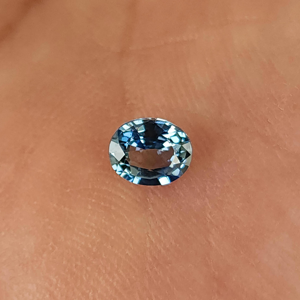 Oval sapphire lying face-up on a palm, with blue edge reflections and skin visible through the center.