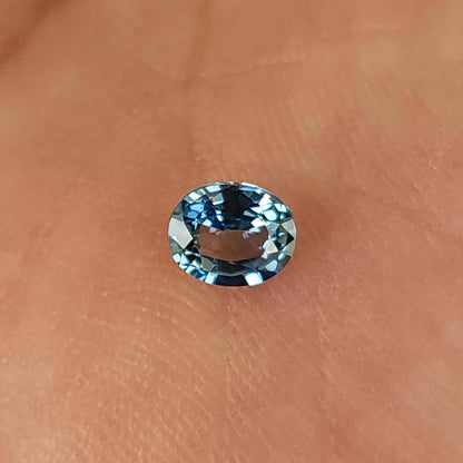 Oval sapphire lying face-up on a palm, with blue edge reflections and skin visible through the center.