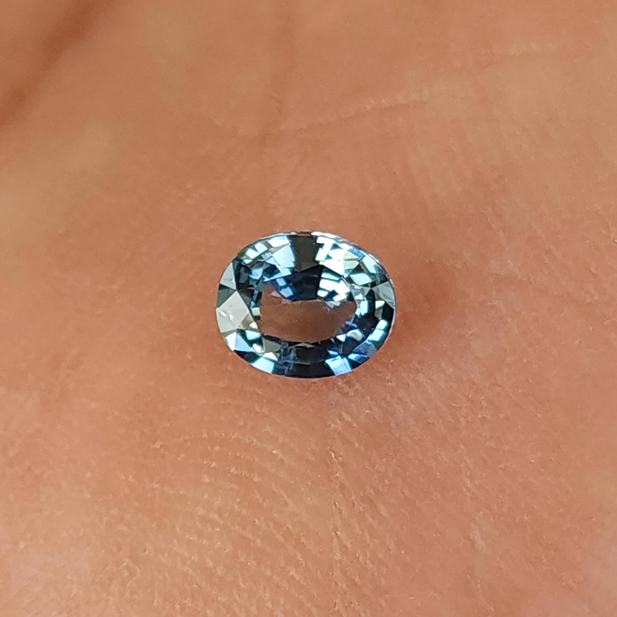 Close angled palm view of the oval sapphire, with pale reflections around the oval rim.