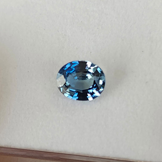 Blue-gray oval sapphire viewed face-up on a white pad, showing its outline and alternating bright and dark facets.