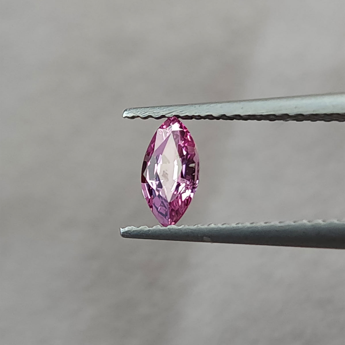 The marquise sapphire rotated in tweezers, with a broad pale reflection across its center.