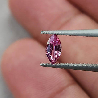 Pink marquise sapphire held upright in tweezers with fingers visible behind it.