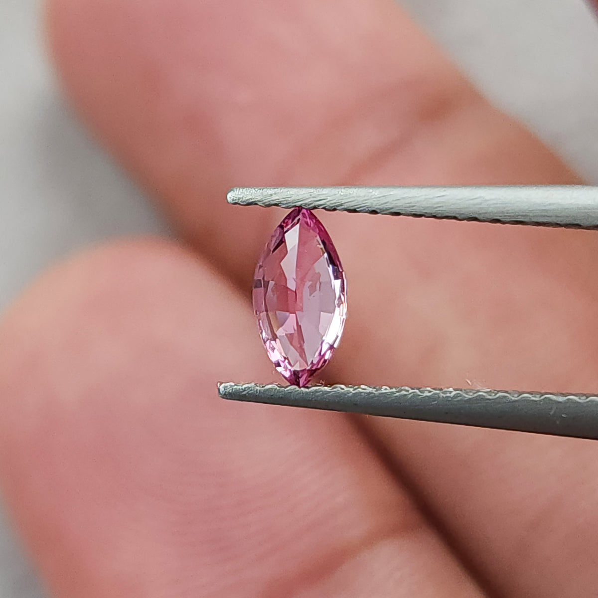 Tilted tweezers view of the marquise sapphire against fingers, showing broad pale central reflections.