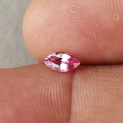 Face-up marquise sapphire between fingertips, showing its pointed ends and alternating bright and pink facets.