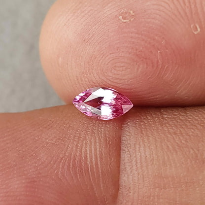 Closer angled fingertip view of the marquise sapphire, with pink edges and a pale central reflection.