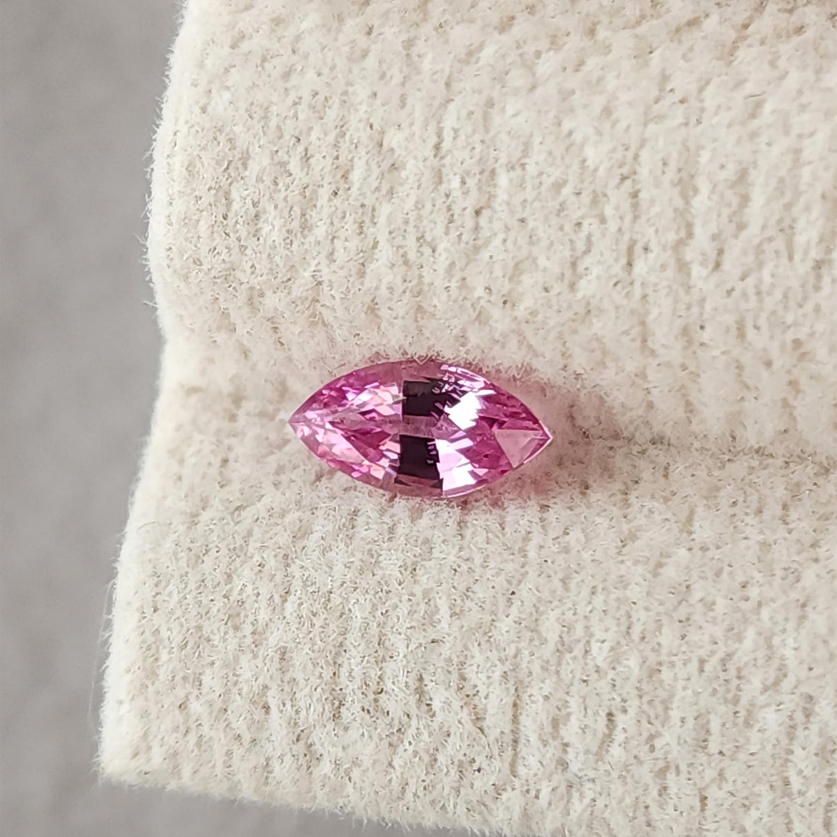Pink marquise sapphire resting horizontally on a cream grooved pad, viewed face-up.