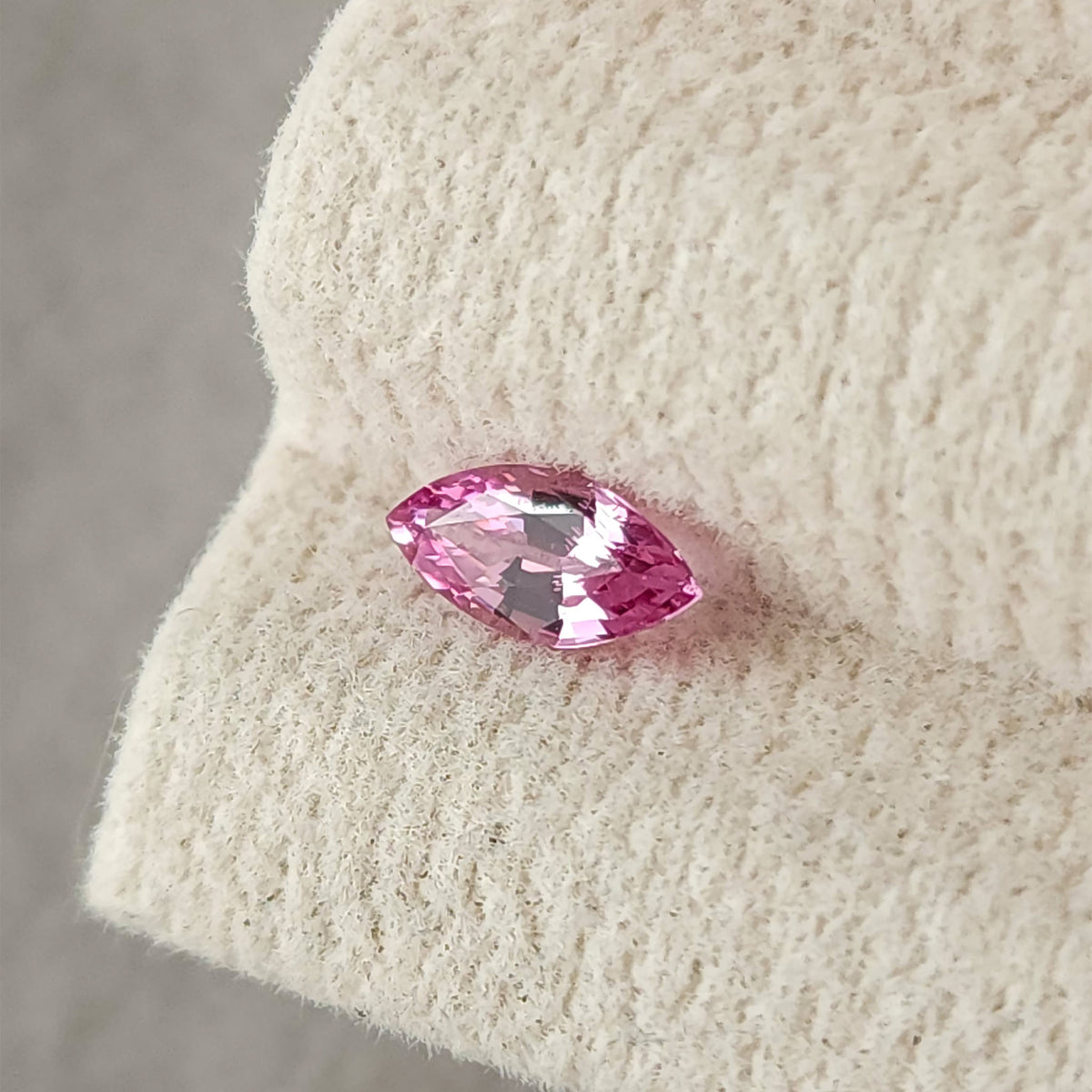 The marquise sapphire on a tilted cream display pad, with pale reflections across several facets.