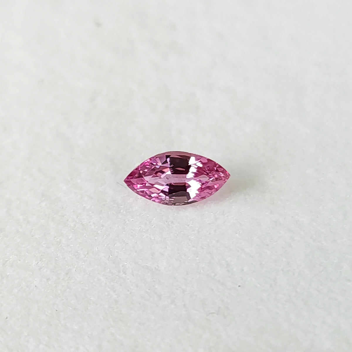 Face-up pink marquise sapphire on a plain white pad, showing both pointed ends and its crown facets.