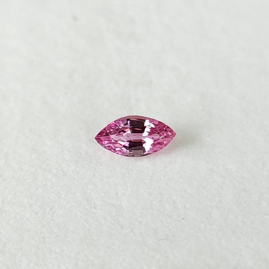 Face-up pink marquise sapphire on a plain white pad, showing both pointed ends and its crown facets.