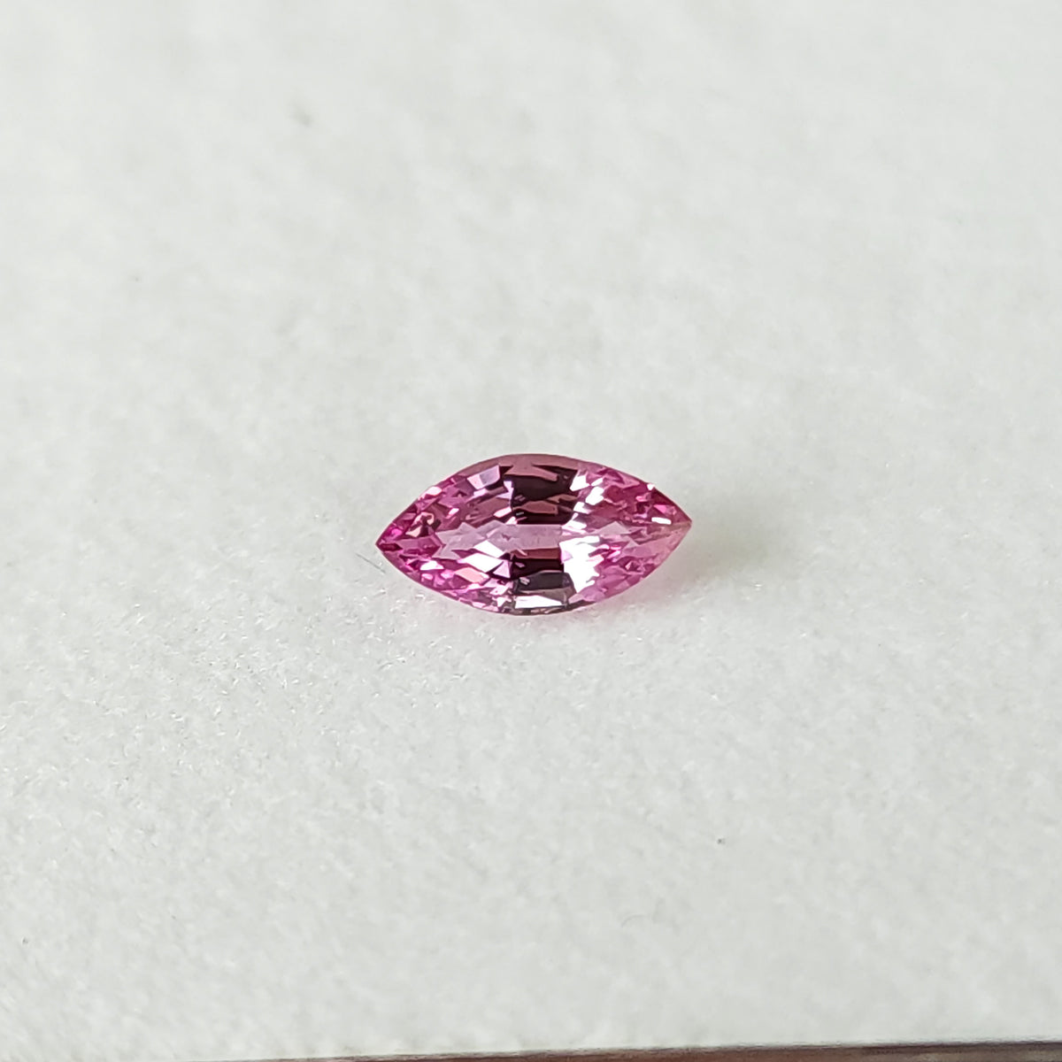 Close alternate face-up view of the pink marquise sapphire on a white pad.