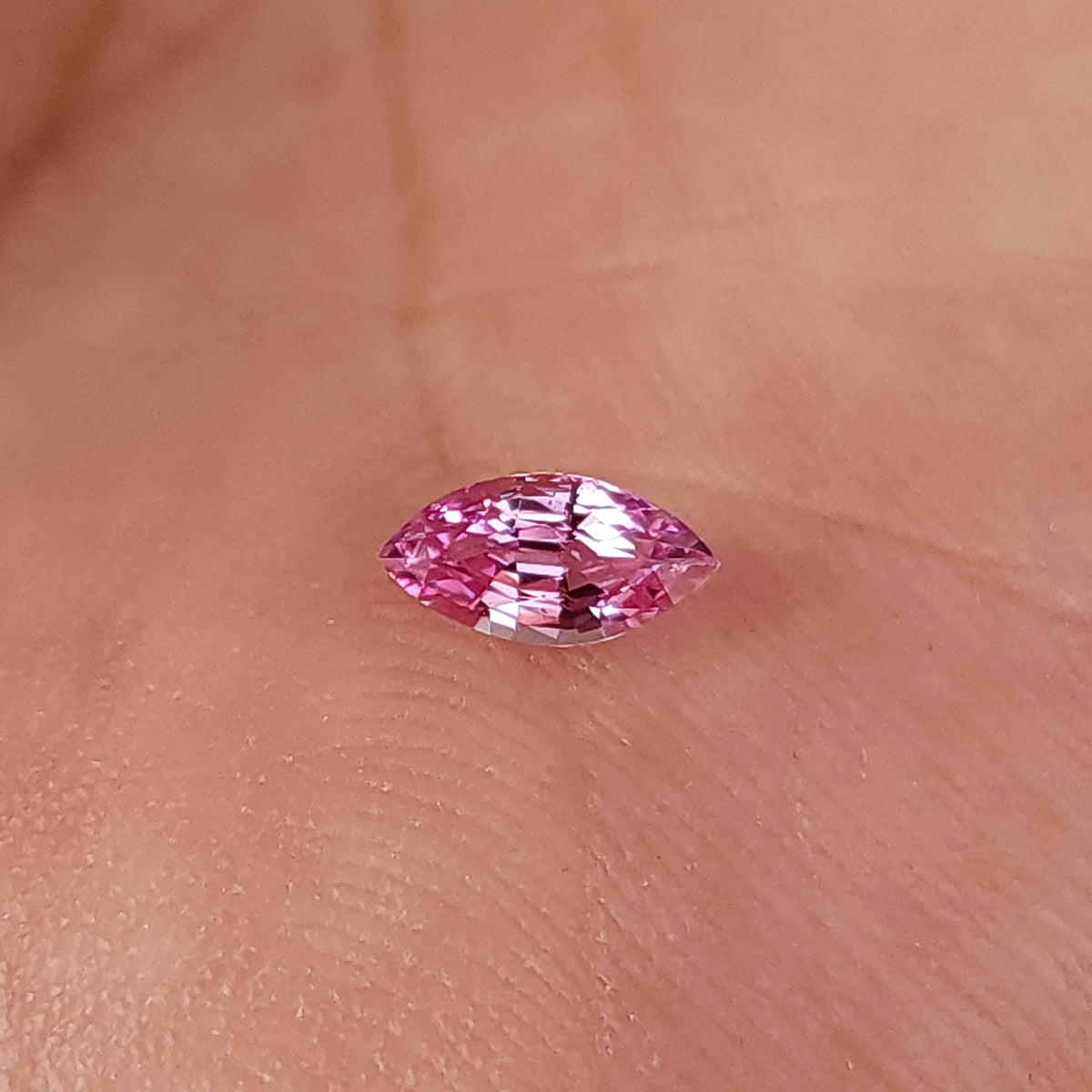 Pink marquise sapphire resting face-up on a palm, showing its small scale against skin texture.