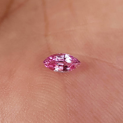Pink marquise sapphire resting face-up on a palm, showing its small scale against skin texture.