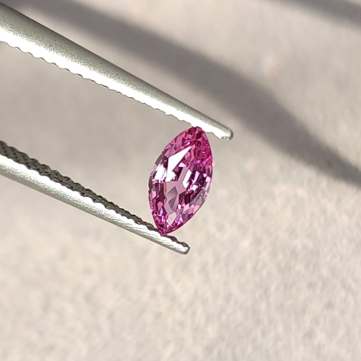 Pink marquise sapphire held diagonally in tweezers at an oblique angle, with the near edge visible.