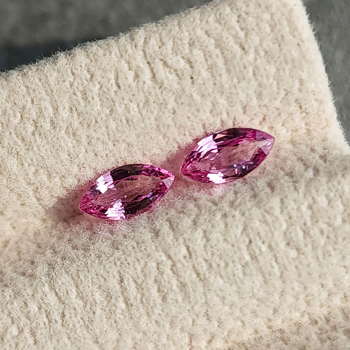 Two pink marquise sapphires arranged diagonally face-up on a cream grooved display pad.