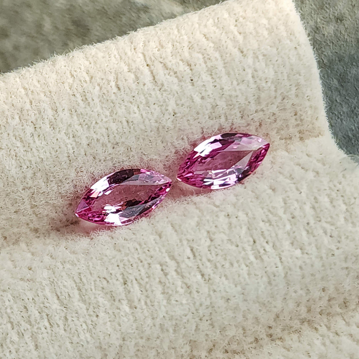 Alternate diagonal cream-pad view of the pink sapphire pair, showing bright reflections near their pointed ends.