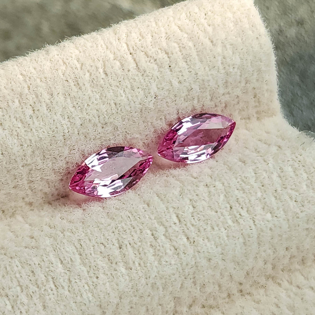 Tilted view of the two marquise sapphires on a cream pad, with pale reflections across their centers.