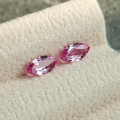 Tilted view of the two marquise sapphires on a cream pad, with pale reflections across their centers.