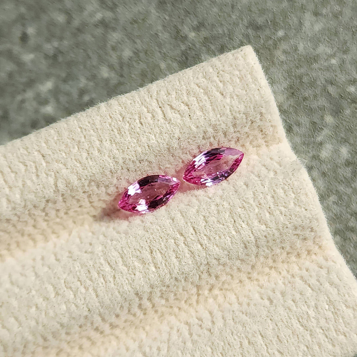 Wider view of the complete sapphire pair on its cream display pad against a gray background.